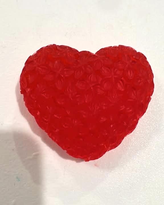 Jabón rojo translúcido en forma de corazón con textura de pequeñas rosas.