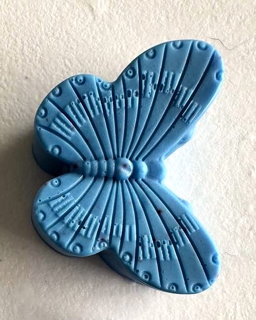 Jabón azul claro en forma de mariposa con las alas en relieve, sobre una superficie blanca.