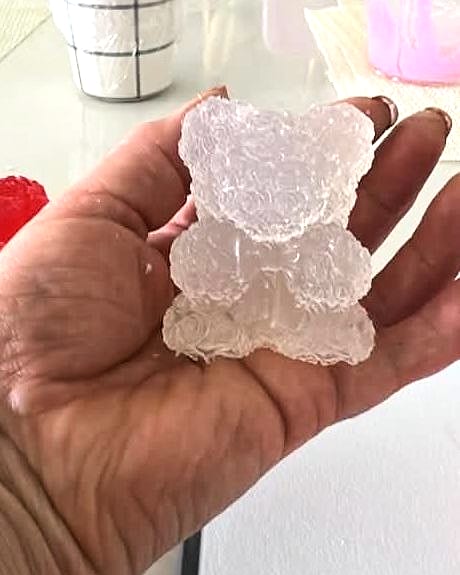 Oso de jabón transparente con textura de rosas, sostenido en la palma de una mano.