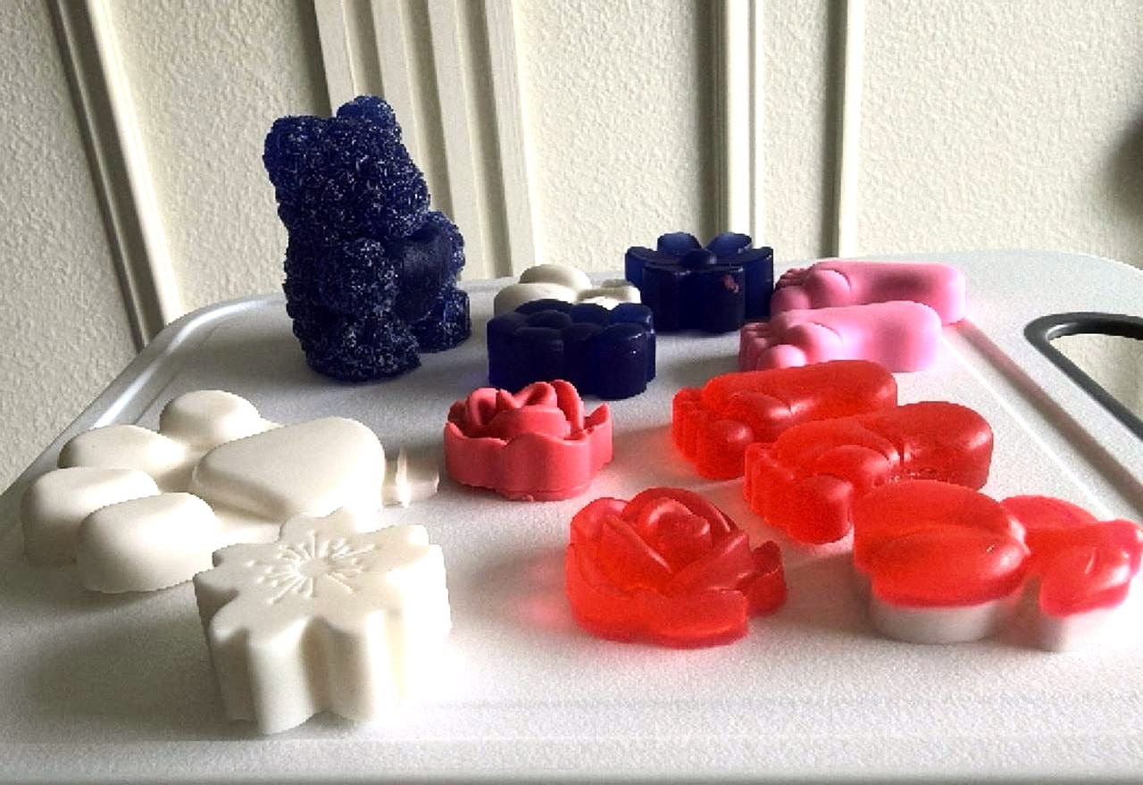 Jabones blancos, rojos, rosados y azules, entre ellos un oso azul, ordenados sobre una bandeja blanca.